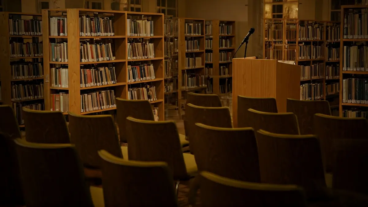 Imaxe xenérica dunha biblioteca con estantes de madeira e un podio con micrófono.